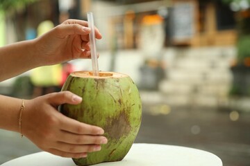 Woman with green coconut of refreshing drink at table outdoors, closeup. Space for text