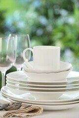 Different clean dishes on white table against blurred green background, closeup