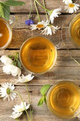 Aromatic herbal tea in glass cups, flowers and green leaves on wooden table, flat lay