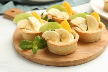 Tartlets with fruits and mint on white table, closeup. Delicious dessert