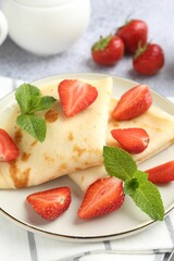 Tasty crepes with strawberries and mint on light gray table, closeup