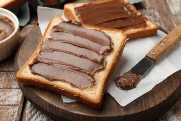Sandwiches with chocolate butter and knife on wooden table, closeup