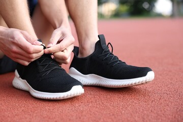 Man tying shoelace of black sneaker at stadium, closeup