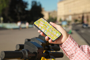 Woman looking at city map on her mobile phone while taking electric kick scooter outdoors, closeup