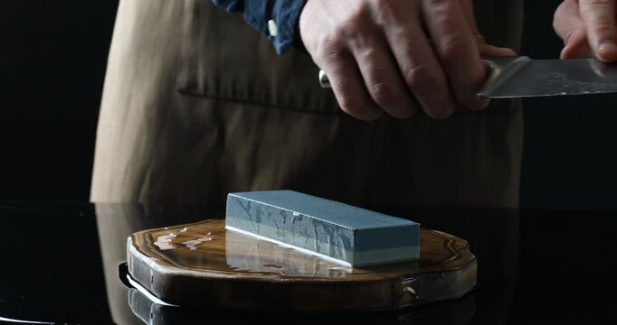 Man sharpening knife with sharpener at mirror table against black background, closeup