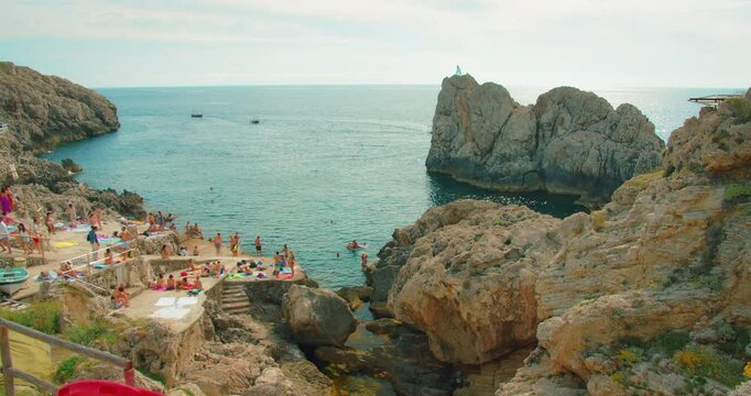 Busy rocky beach Punta Carena with people sunbathing and swimming in summer Capri