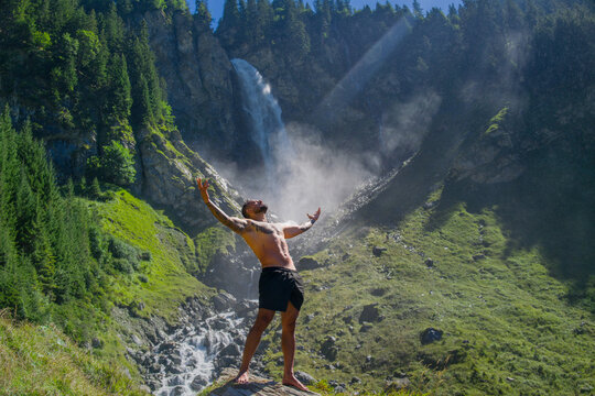 Muscular guy breathing fresh air. Handsome topless model with raised hands breathing air. Sexy man meditating on nature. Calm breathing air by the waterfall. Wellness and breathing in nature.