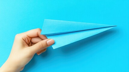 Hand holding a blue paper airplane against bright blue backgroun