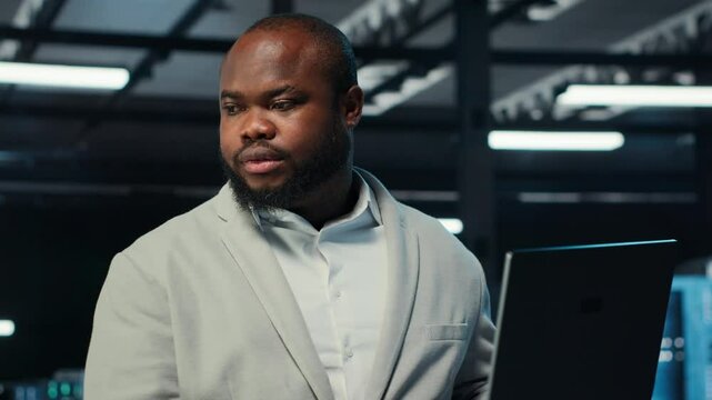 Data center system administrator coding on laptop, doing software updates. Server room IT specialist looking at device screen, optimizing infrastructure rackmounts configuration rigs, camera B