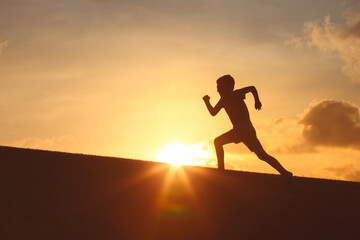 Silhouette of a child boy running in a field with a stunning sunset backdrop. Healthy active childhood concept 