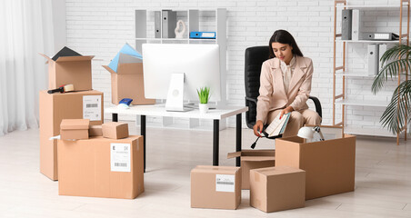 Fototapeta premium Young businesswoman packing things in office on moving day