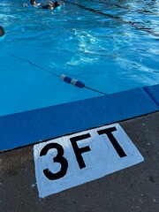 swimming pool depth sign - The shallow end of a pool with a 3 foot depth sign painted on the concrete - edge of swimming pool, blue water and a safety rope. Low angle view of public swim park