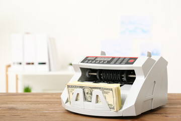 Modern cash counting machine with dollar banknotes on table in office