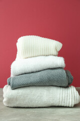 Stack of different light stylish sweaters on color background