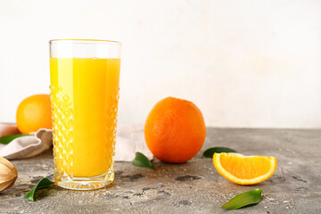 Glass of fresh orange juice with wooden juicer and leaves on grey table