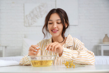 Young Asian woman preparing steam inhalation with herbs at table in bedroom