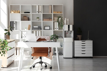 Interior of office with workplace, shelf unit and water cooler