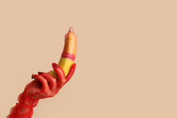Female hand in red glove with banana and condom on color background, closeup. Erotic concept