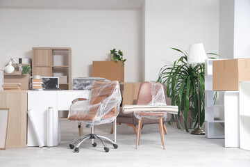 Interior of office with desk, boxes and wrapped chairs in stretch film on moving day