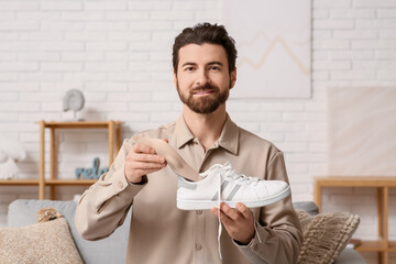 Young man putting beige orthopedic insole into sneaker at home