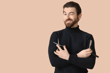 Bearded young man with straight razor and scissors winking on beige background