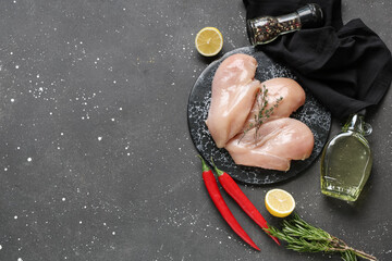 Board with raw chicken breast and different spices on black background