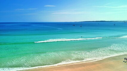 A stunning view of a tranquil tropical beach with clear turquoise waters and soft waves under a blue sky.