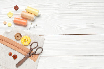 Different colorful buttons with thread spools, fabric sample and scissors on white wooden background