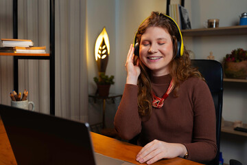 Redhead woman enjoying music with headphones while working from home. A relaxed and cheerful moment...