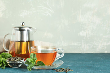 Glass cup and teapot of hot mint tea with dry leaves on green background