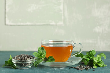 Glass cup of hot mint tea and bowl with dry leaves on green background