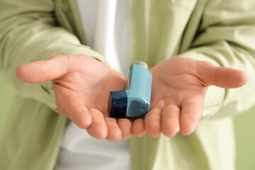 Young man with inhaler on green background, closeup