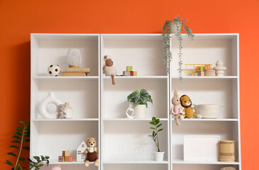 Shelf unit with toys and plants near orange wall in children's room