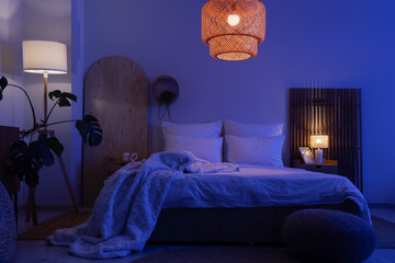 Interior of dark room with bed, tables and glowing lamps at night