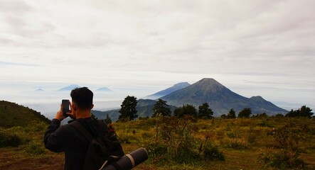A man is capturing the moment by photographing a mountain with a cellphone