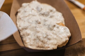 Rustic southern biscuits smothered in creamy sausage gravy in takeaway tray, close-up food photography