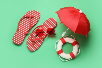 Composition with stylish flip-flops, sunglasses, decorative lifebuoy and umbrella on green...