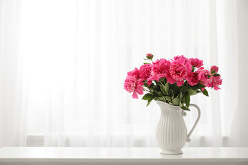 Vase with beautiful pink peony flowers on table near window in room, closeup