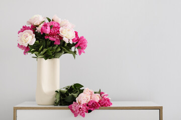 Vase with beautiful peony flowers on chest of drawers near white wall in interior of room, closeup