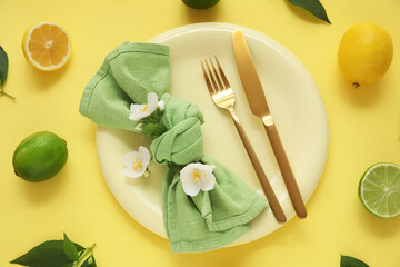 Beautiful table setting with plate, golden cutlery, citrus fruits and flowers on yellow background, closeup