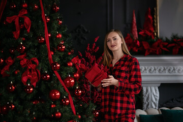 A beautiful young woman in a red plaid shirt with a gift near the Christmas tree. Christmas mood. 