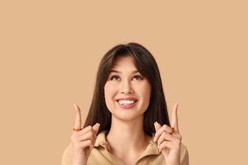 Smiling young woman pointing at something on beige background, closeup