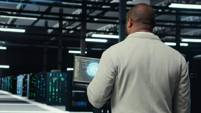 Technician using laptop in data center, managing server virtualization, running scripts. IT expert using programming language on notebook in server hub, finetuning network protocols, camera B