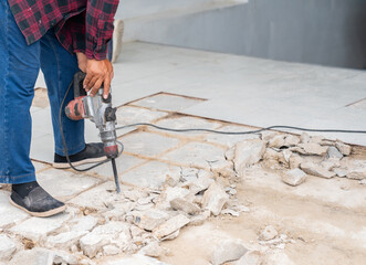 The worker is using a jackhammer to remove the old tiled concrete floor.