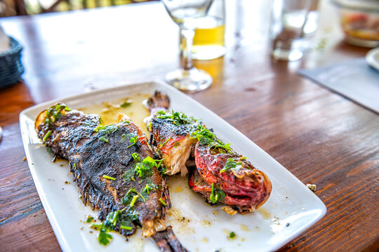 Red scorpionfish scorpion fish seafood dish meal on white plate, table at restaurant on Ikaria island, Greece Greek homemade wine in background