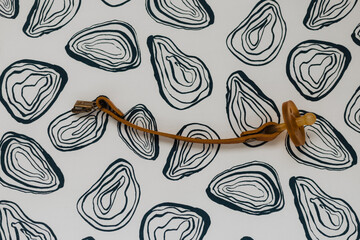 Brown leather pacifier clip with amber silicone soother on black-and-white abstract patterned background, modern minimalist baby accessory flat-lay product shot