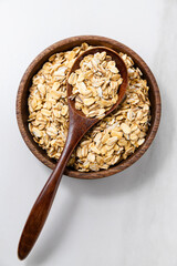 Top view of a wooden bowl with rolled oats and a wooden spoon