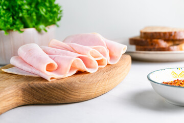 Close-up of sliced turkey ham arranged in elegant folds on a wooden cutting board. Fresh sandwich...