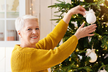 Smiling elderly woman decorating Christmas tree. kitchen interior, copy space. Beautiful old lady...