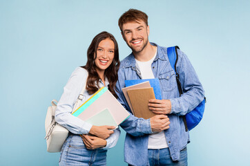 Happy young student couple in denim, with man wearing backpack and holding books, and woman...